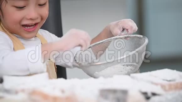 可爱的亚洲小男孩在家厨房里用筛子筛面粉准备烘焙面包店和c视频的预览图