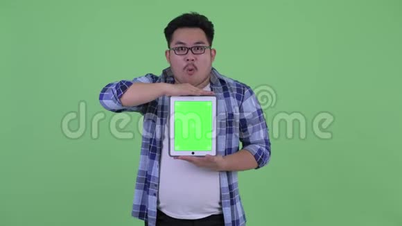 年轻快乐体重超重的亚洲时髦男人展示数码平板电脑看上去很惊讶视频的预览图