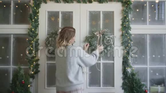 穿暖和毛衣的女人用圣诞花环装饰大门装饰圣诞屋舒适的新房子视频的预览图