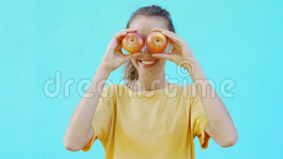 漂亮的微笑女孩正在五颜六色的明亮的青色背景上摆姿势并展示了新鲜成熟美味的黄红色苹果妇女视频的预览图