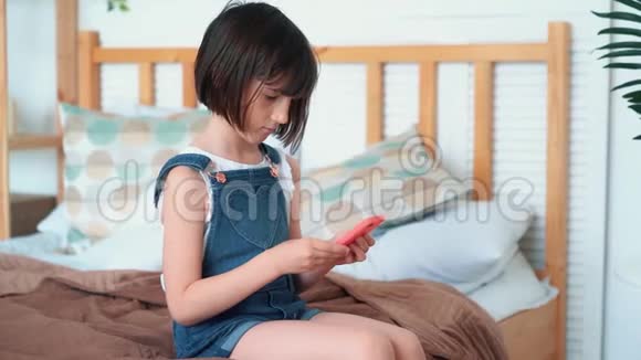 小可爱坐在床上用智能手机玩游戏慢动作视频的预览图