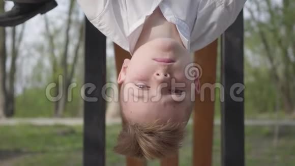 十几岁的男孩把头从横杆上垂下来在春天公园的背景下微笑着视频的预览图