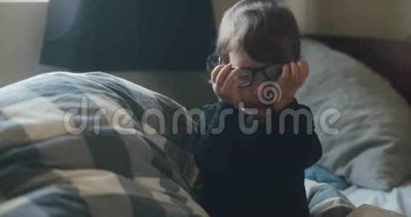 有趣的小女孩戴着父母的眼镜在床上视频的预览图
