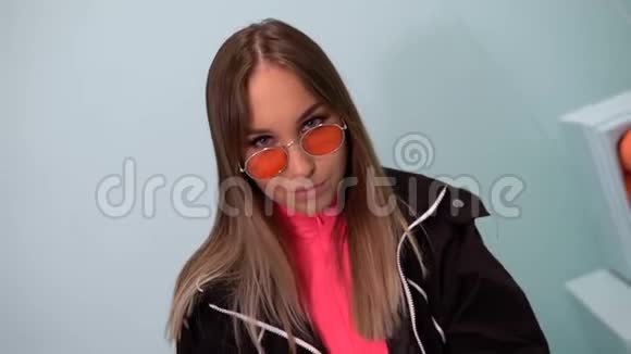 戴绿松石背景眼镜的时髦女孩坐在椅子上床头柜上的橘子视频的预览图