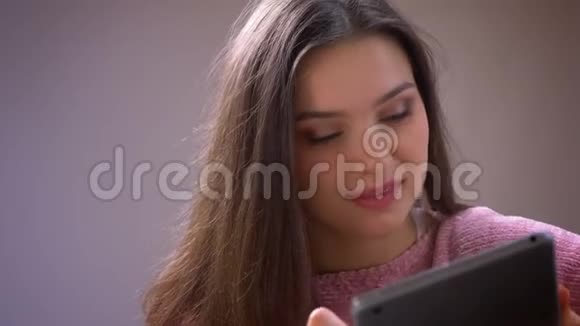 一位年轻漂亮的黑发白种人女性在平板电脑上愉快地微笑着看着镜头的特写镜头视频的预览图