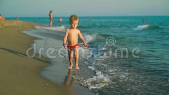 快乐的男孩快乐地跑着跳着在夕阳下溅在海水里慢动作视频的预览图