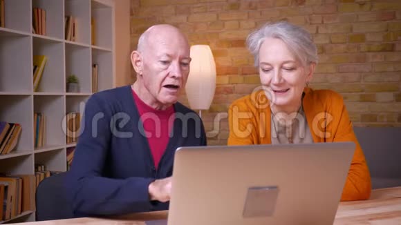 年长的白发白种人夫妇在办公室的笔记本电脑前愉快地交谈视频的预览图
