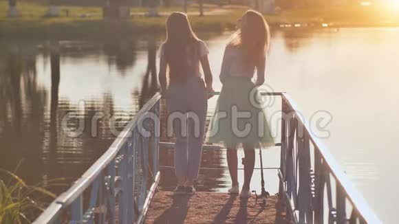 日落时分两个金发女孩和女朋友背对着湖边视频的预览图