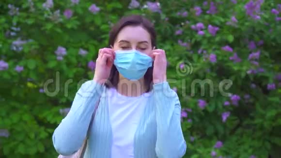 一位年轻女子的肖像摘下她的医用面具在花朵的背景下深深地呼吸着空气视频的预览图