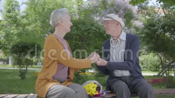 在公园的长凳上一位老太太手拿一束黄花和一位老人坐在一起招标视频的预览图