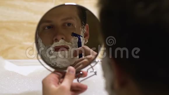 漂亮的年轻男人在浴缸里刮胡子照镜子男人的美容仪式视频的预览图