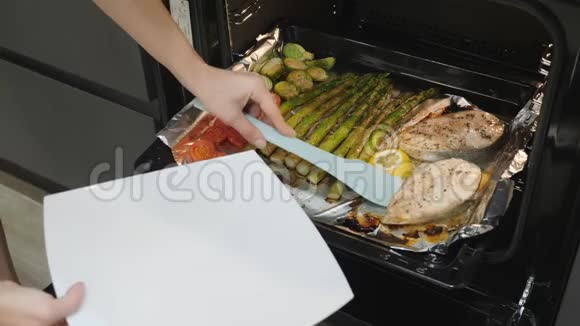 厨师把鲑鱼从烤箱里弄出来女人准备浪漫美味的晚餐带西红柿芽甘蓝和煮熟的鱼排视频的预览图