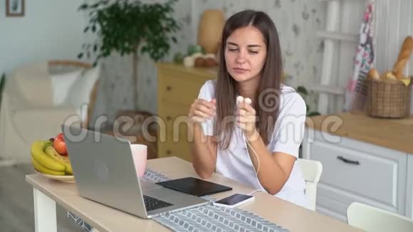 女孩在笔记本电脑上工作戴上耳机打开手机上的音乐慢动作视频的预览图