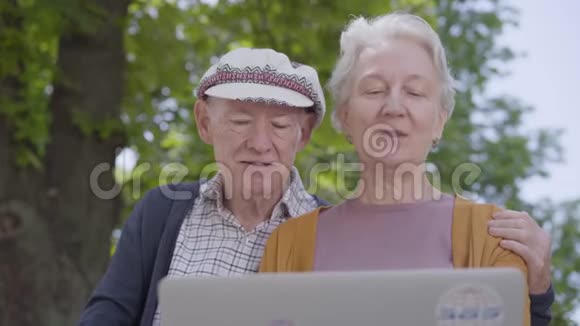 肖像可爱的老女人白发苍苍戴着帽子的老人坐在美丽的公园里的长凳上和他说话视频的预览图