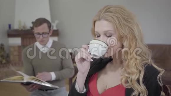 美丽的金发女人在前台喝咖啡而穿着端庄的男人在后台读这本书视频的预览图