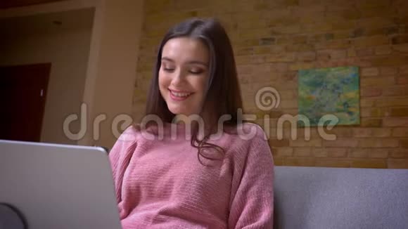 一位年轻漂亮的棕色白种人女商人在笔记本电脑上工作坐在沙发上微笑的特写镜头视频的预览图