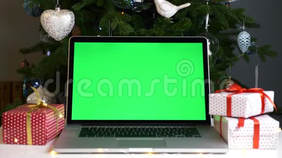 带有绿色屏幕的笔记本电脑放在圣诞礼物盒和圣诞树上视频的预览图
