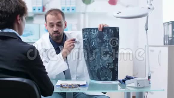 现代研究设施的办公桌上的医生向病人展示X光扫描视频的预览图