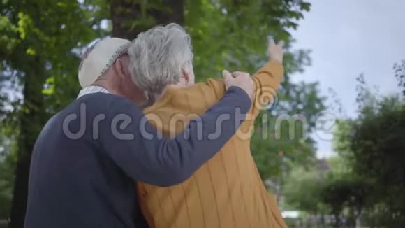 戴着帽子的老人背着一位白发苍苍的女人在令人惊叹的绿色公园里视频的预览图