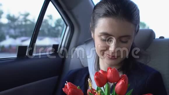 快乐的女孩坐在车里闻花满意的出租车客户享受乘车视频的预览图