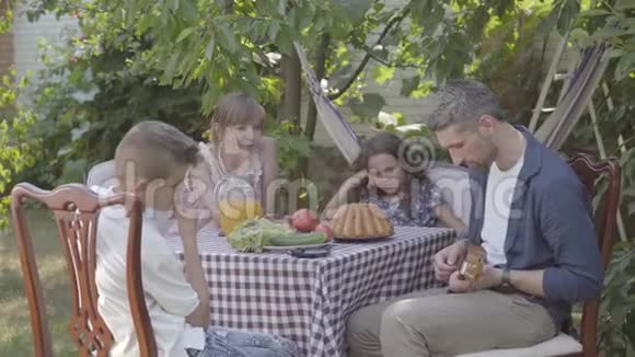 父亲坐在后院的餐桌上为家人弹吉他友好的家庭关系视频的预览图