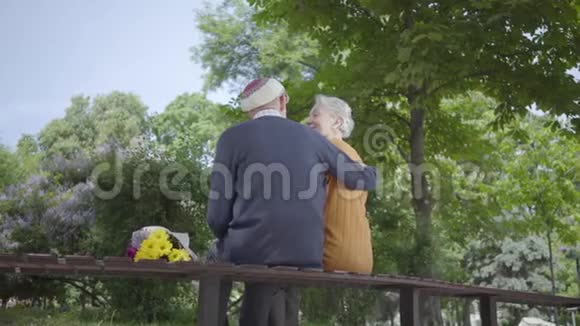 老人的背坐在公园的长凳上捧着一束黄色的花抱着一个白发的女人女人让她视频的预览图