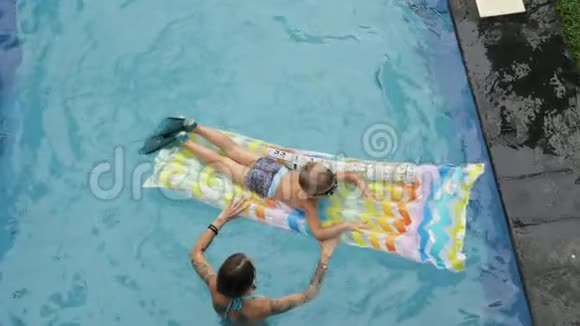 小男孩和妈妈在亚洲度假的游泳池里游泳婴儿游泳妈妈和儿子在床垫上的游泳池里游泳视频的预览图