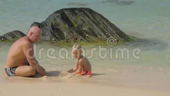 小男孩和爸爸在冲浪线上玩干净的湿沙视频的预览图