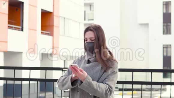 城市街道上的年轻女孩戴着黑色无菌医疗面罩用餐巾纸擦拭手机女人用电话视频的预览图
