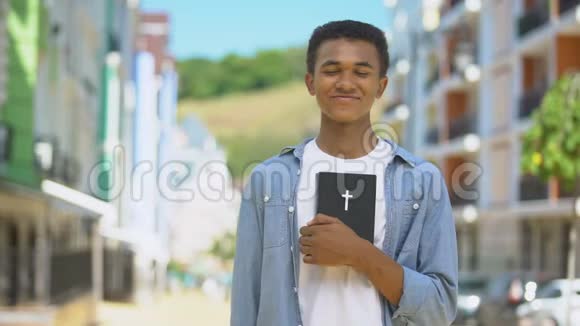 快乐的混血年轻人拿着神圣的圣经在卡姆宗教上微笑视频的预览图