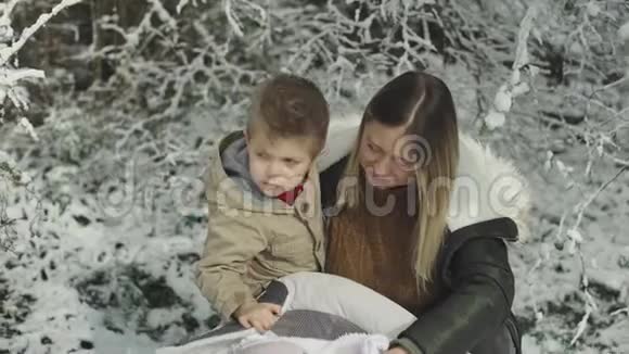 年轻时尚的妈妈和她可爱的女儿和儿子在冬天的雪公园视频的预览图