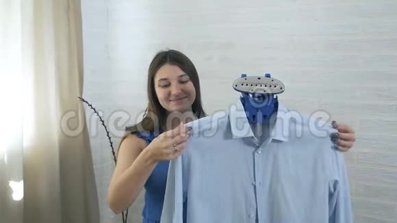 年轻的女人微笑着用蒸汽抚摸男人衬衫蒸汽蒸衣服的过程视频的预览图