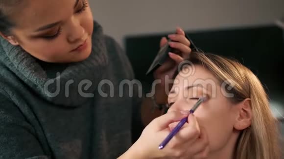 亚洲化妆艺术家化妆用画笔描绘眼睛上的阴影在此背景下视频的预览图