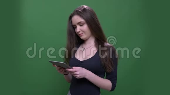 用平板电脑拍摄的年轻漂亮黑发女性的特写肖像并愉快地微笑着背景与绿色隔离视频的预览图