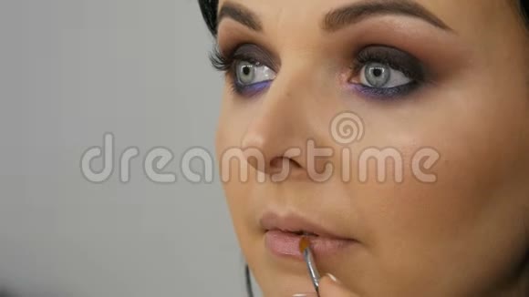 蓝眼睛淡紫色专业化妆烟熏眼睛化妆师的年轻女子令人惊叹的美丽面容视频的预览图