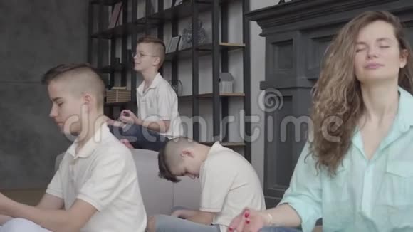 年轻漂亮的母亲坐在客厅里她的三个十几岁的儿子一起冥想女人和她的孩子在一起视频的预览图