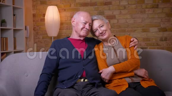 年长的白种人夫妇坐在沙发上互相拥抱在家里对着镜头微笑视频的预览图