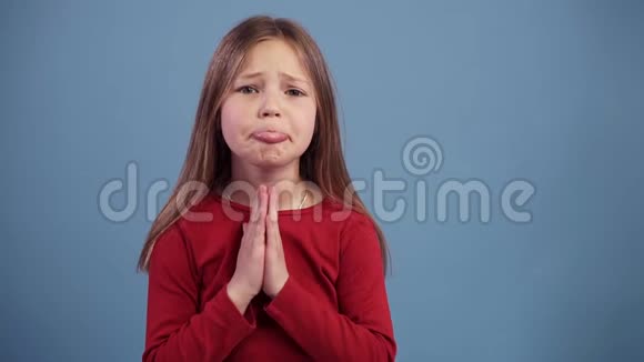 年轻美丽的白种人金发女孩乞求说请在蓝色背景上缓慢地祈祷穿着红色衣服视频的预览图