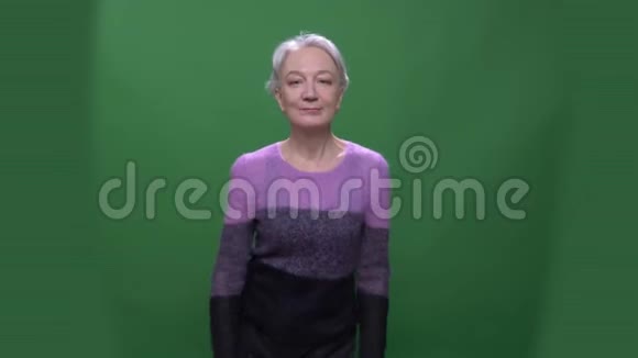 穿着紫色毛衣的灰头发老年妇女在绿色的色彩背景下谦逊地跳舞视频的预览图
