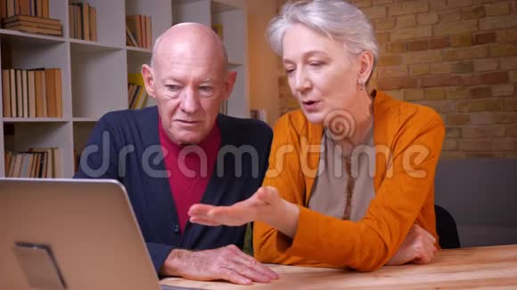 两位白发苍苍的白种人高级配偶在笔记本电脑上用视频聊天的特写镜头积极地打手势视频的预览图