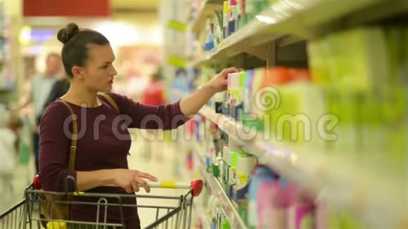 年轻女性从超市货架上挑选假发一个有白人外表的女孩在超市买东西高清高清视频的预览图