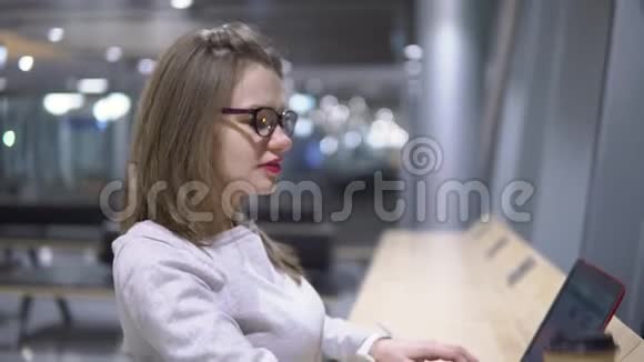 年轻漂亮的女孩正站在一张桌子旁手提电脑旁端着纸杯喝着咖啡视频的预览图