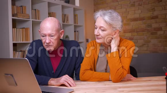两位年长的白发白种人同事在笔记本电脑上用视频聊天讨论办公室里的项目视频的预览图