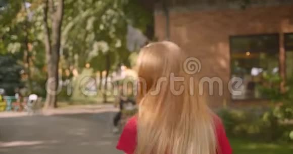 近景后景照片年轻的金发碧眼的美丽女性步行到公园的咖啡馆视频的预览图
