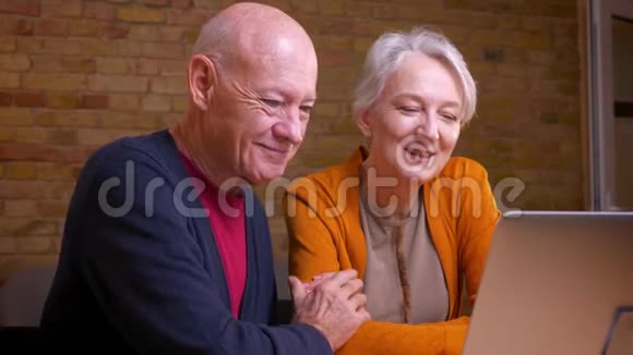 两位年长的白发白种人配偶在笔记本电脑上用视频聊天彼此温柔地拥抱视频的预览图
