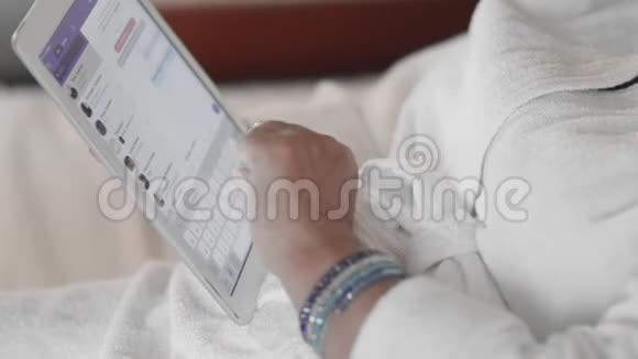 一位穿着白色特里长袍躺在床上的老妇人使用平板电脑在信使上写了一条信息动作缓慢接近视频的预览图