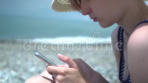 漂亮的年轻女人在海边使用智能手机穿着复古帽子和蓝白条纹泳衣的女孩视频的预览图