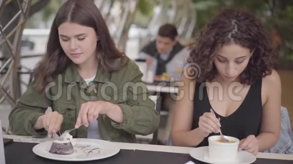 两个年轻女人坐在户外咖啡馆里吃蛋糕的肖像年轻的女孩一起享受着晚餐的谈话视频的预览图