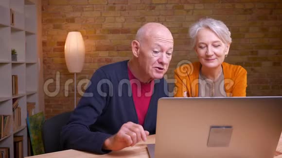 两位白发苍苍的老白种人配偶的肖像在笔记本电脑上用视频聊天在办公室里很开心视频的预览图