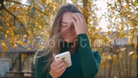 有趣的年轻迷人的黑发女人使用智能手机和微笑的背景黄树在秋天视频的预览图